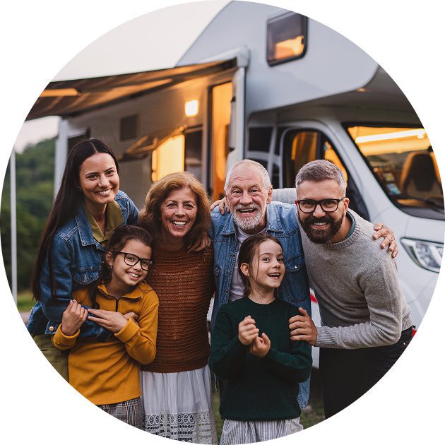 image A family of six, including two children and four adults, stands together smiling in front of a camper van parked outdoors.